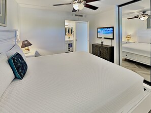A bedroom with a large bed, a ceiling fan, a TV, and a wardrobe.