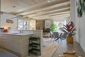 A modern kitchen with a wooden ceiling, a dining area with a table and chairs, and a living space with a TV and plants. - Luderna - Apartamento Val de Ruda A30 Manaud (Baqueira)