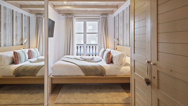 Een slaapkamer met twee bedden, houten balken in het plafond, een groot raam en uitzicht op het omliggende landschap.