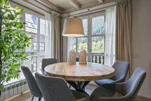 A round wooden table with four chairs, a hanging light fixture, and two woven candle holders. - Luderna - Apartamento Val de Ruda A30 Manaud (Baqueira)