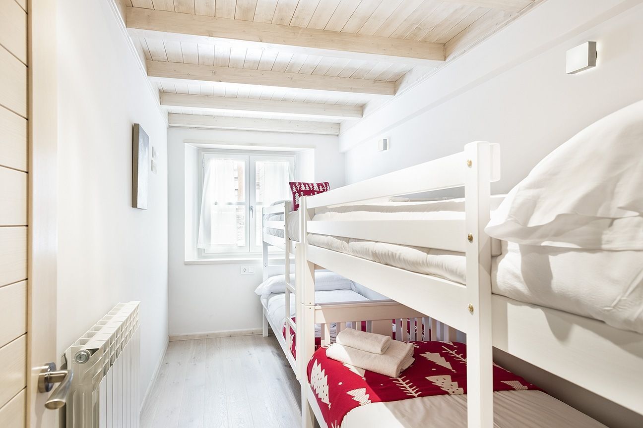 A narrow room with bunk beds, a radiator, and a window with curtains.