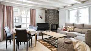 Een moderne woonkamer met een stenen open haard, een eethoek met een tafel en stoelen, en een groot raam met gordijnen.