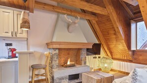 Een gezellige kamer met een stenen open haard, houten balken, een houten plafond en een decoratie van een hertenkop.