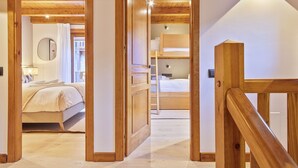Hotelkamer met houten vloer, een bed, nachtkastje en bijzettafeltje. Er is een raam met gordijnen, en een deur die naar een andere kamer leidt.