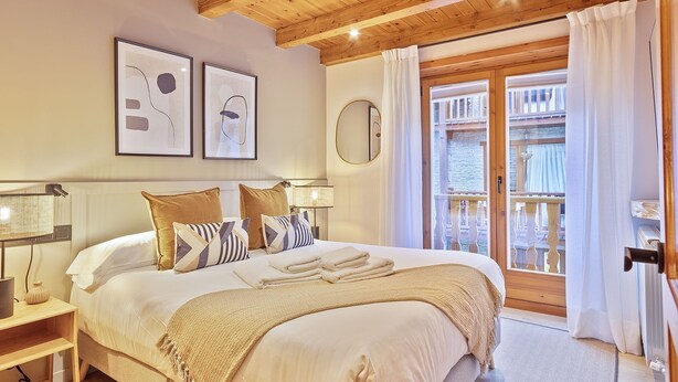 Een slaapkamer met een groot bed, een houten plafond, een balkon met een balustrade en kunstwerken in lijsten aan de muur.