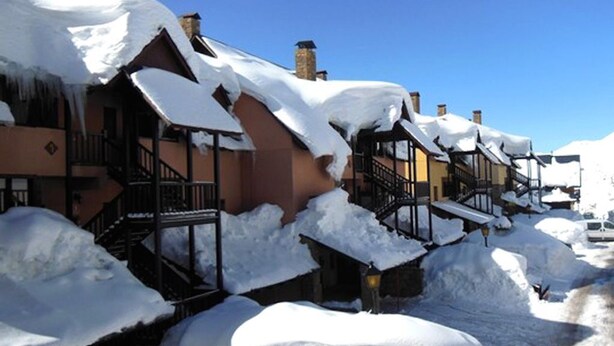 A row of snow-covered buildings with balconies and a clear blue sky.