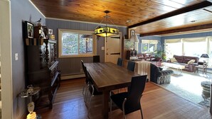 A spacious dining area with a wooden table and chairs, a chandelier, and a view of the outdoors through a large window. - Streamside dream with hot tub (Idaho Springs)