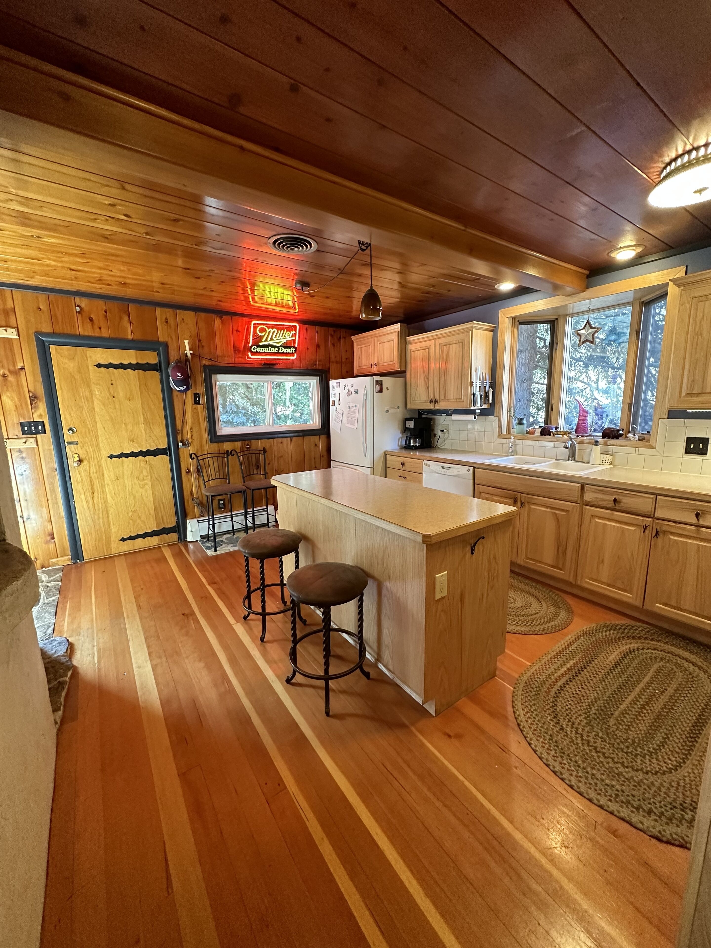 A wooden cabin interior with a kitchen featuring a bar area, wooden cabinets, and a refrigerator.