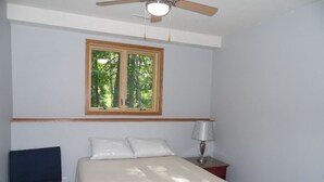 A bedroom with a bed, a chair, a nightstand, a lamp, and a ceiling fan. - Cardinal Crest of Sister Bay (Sister Bay)