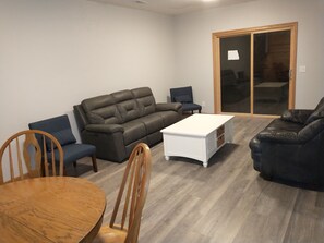 A living room with a grey sofa, a white coffee table, and a wooden dining table with chairs.