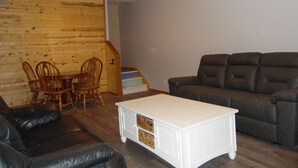 A living room with a brown leather sofa, a white coffee table with storage, a dining table with chairs, and a staircase leading to an upper level. - Cardinal Crest of Sister Bay (Sister Bay)