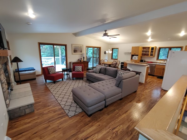 A spacious living area with a grey sectional sofa, red armchairs, a wooden floor, and a kitchen area with wooden cabinets and a white refrigerator. - Cardinal Crest of Sister Bay (Sister Bay)