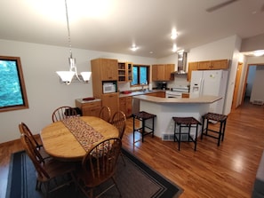 A modern kitchen with wooden cabinets, a central island, and a dining area with a round table and chairs. - Cardinal Crest of Sister Bay (Sister Bay)