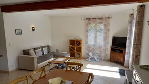 Ein Wohnzimmer mit Sofa, Fernseher, einem Holzschrank und einem Essbereich mit Tisch und Stühlen.