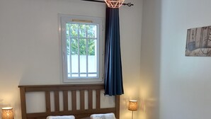 Ein Schlafzimmer mit einem hölzernen Bett, zwei Nachttischlampen, einem Fenster mit Vorhängen und einer Pendelleuchte.