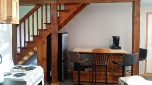 A kitchen with a wooden staircase, a stove, a refrigerator, and a coffee maker on a table.