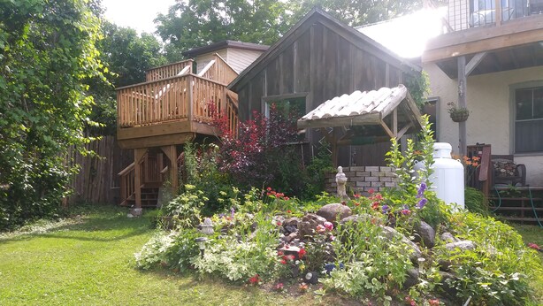 A wooden house with a deck and a garden with various plants and flowers.