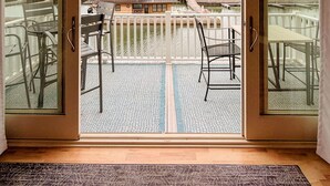A room with a large sliding glass door leading to a balcony with outdoor seating and a view of a residential area. - Gorgeous Townhouse & Boathouse in Cozy Carnegie Bay (Alexandria Bay)
