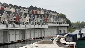 A row of multi-story buildings with uniform architecture, a dock with boats, and a calm water body. - Gorgeous Townhouse & Boathouse in Cozy Carnegie Bay (Alexandria Bay)