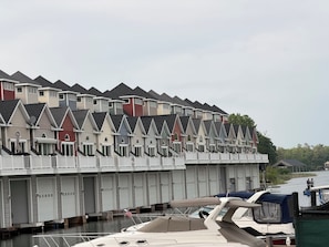 A row of multi-story buildings with uniform architecture, a dock with boats, and a calm water body.