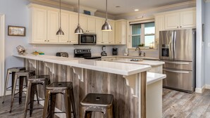 A modern kitchen with white cabinets, stainless steel appliances, and a central island with stools. - Two Palms | Your Gulf-Front Happy Place. Pets Welcome (Dauphin Island)