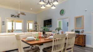 A dining area with a wooden table, white chairs, and a ceiling fan. - Two Palms | Your Gulf-Front Happy Place. Pets Welcome (Dauphin Island)