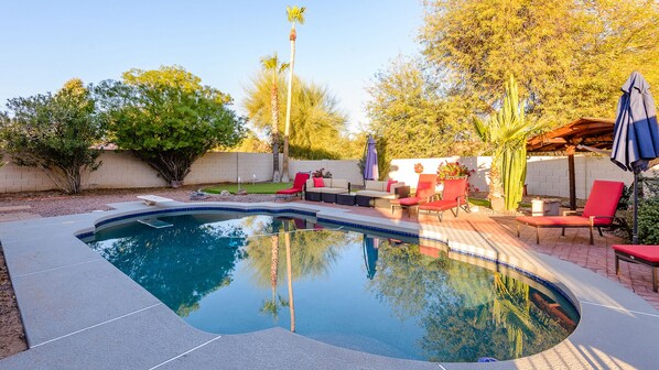 A swimming pool with a curved edge, surrounded by a patio area with red chairs and a covered seating area.