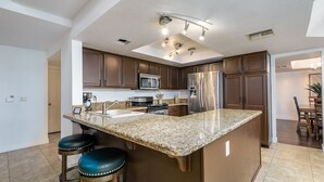 A modern kitchen with granite countertops, stainless steel appliances, and a central island with bar stools. - Family-Friendly Retreat, Heated Pool, Putting Green (Scottsdale)
