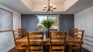 A dining room with a wooden table and chairs, a chandelier, and a window with blinds. - Family-Friendly Retreat, Heated Pool, Putting Green (Scottsdale)