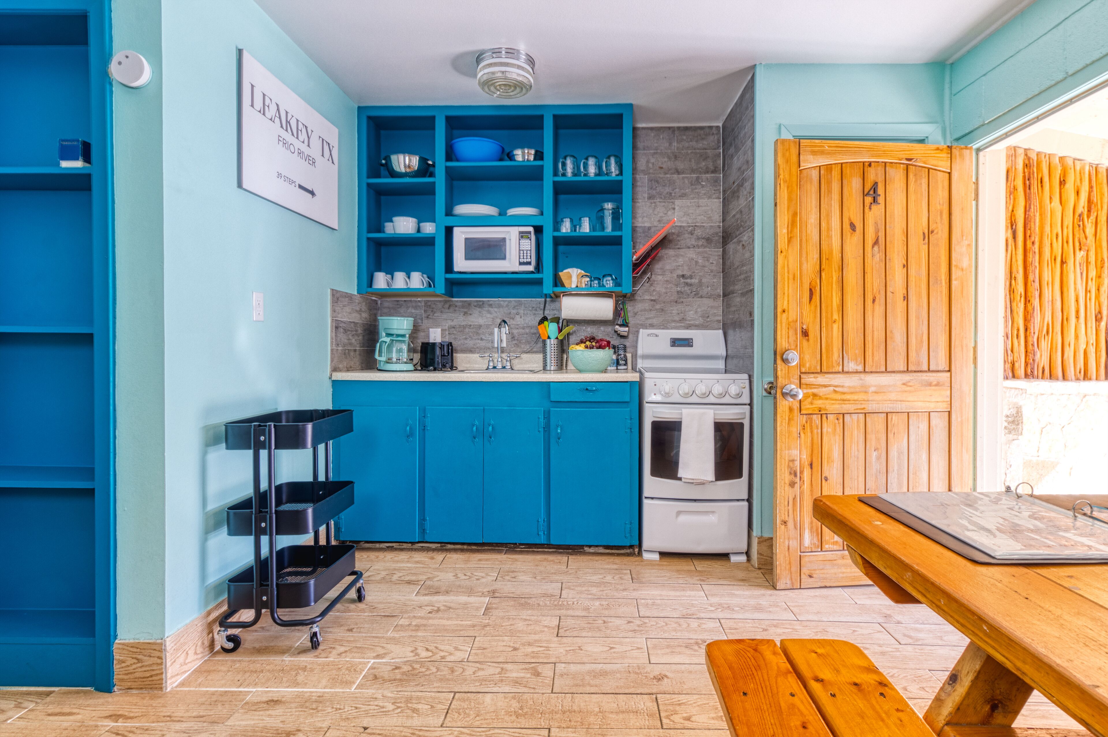 Une cuisine avec des armoires bleues, un four à micro-ondes, une cuisinière et une porte en bois.