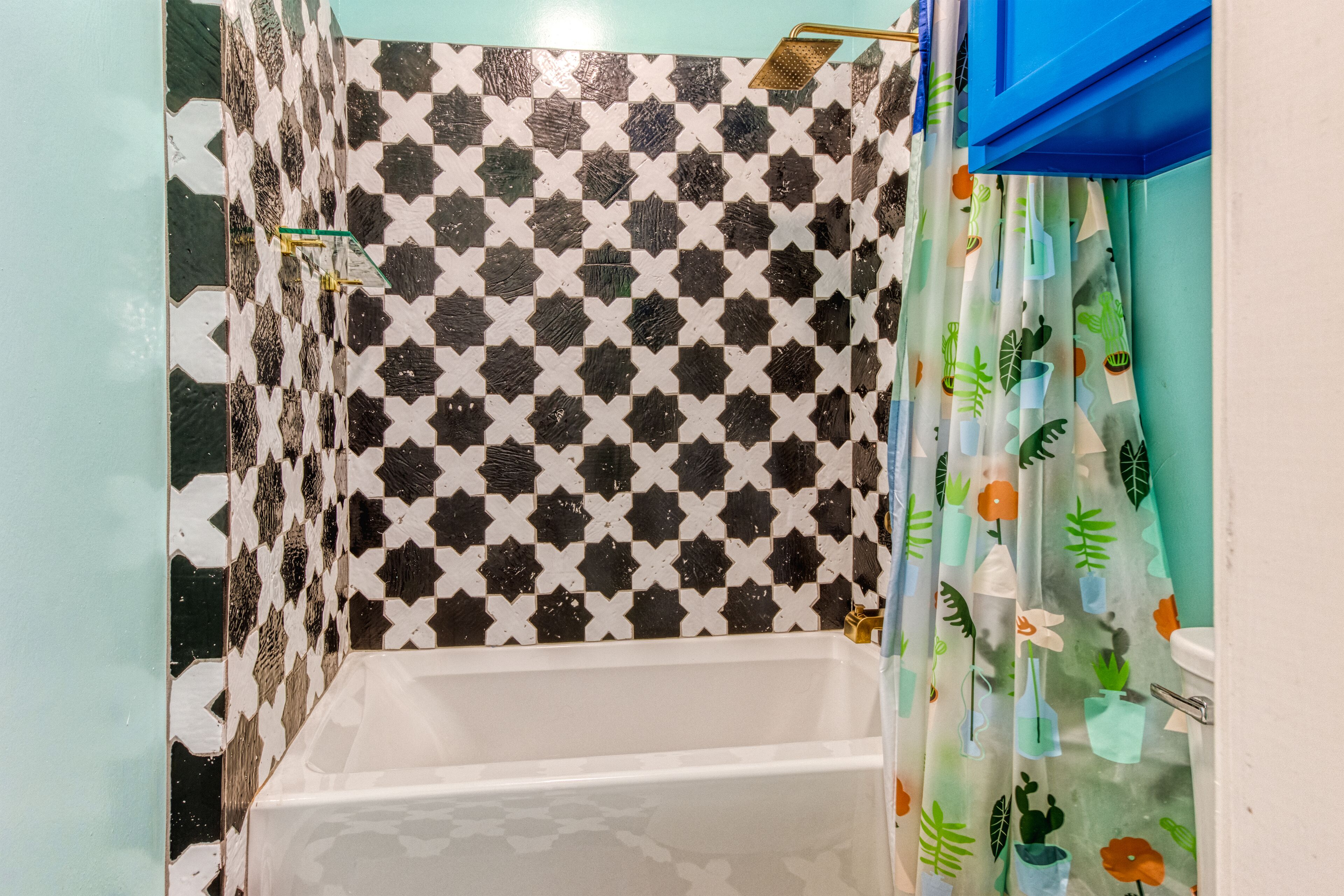 A bathroom with a checkered tile wall, a white bathtub, and a shower curtain with a plant pattern.