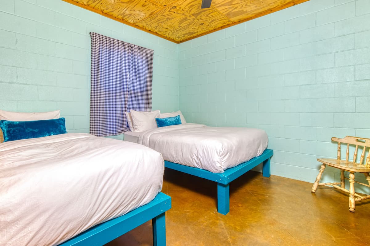 A room with two beds, a wooden chair, and a checkered curtain.