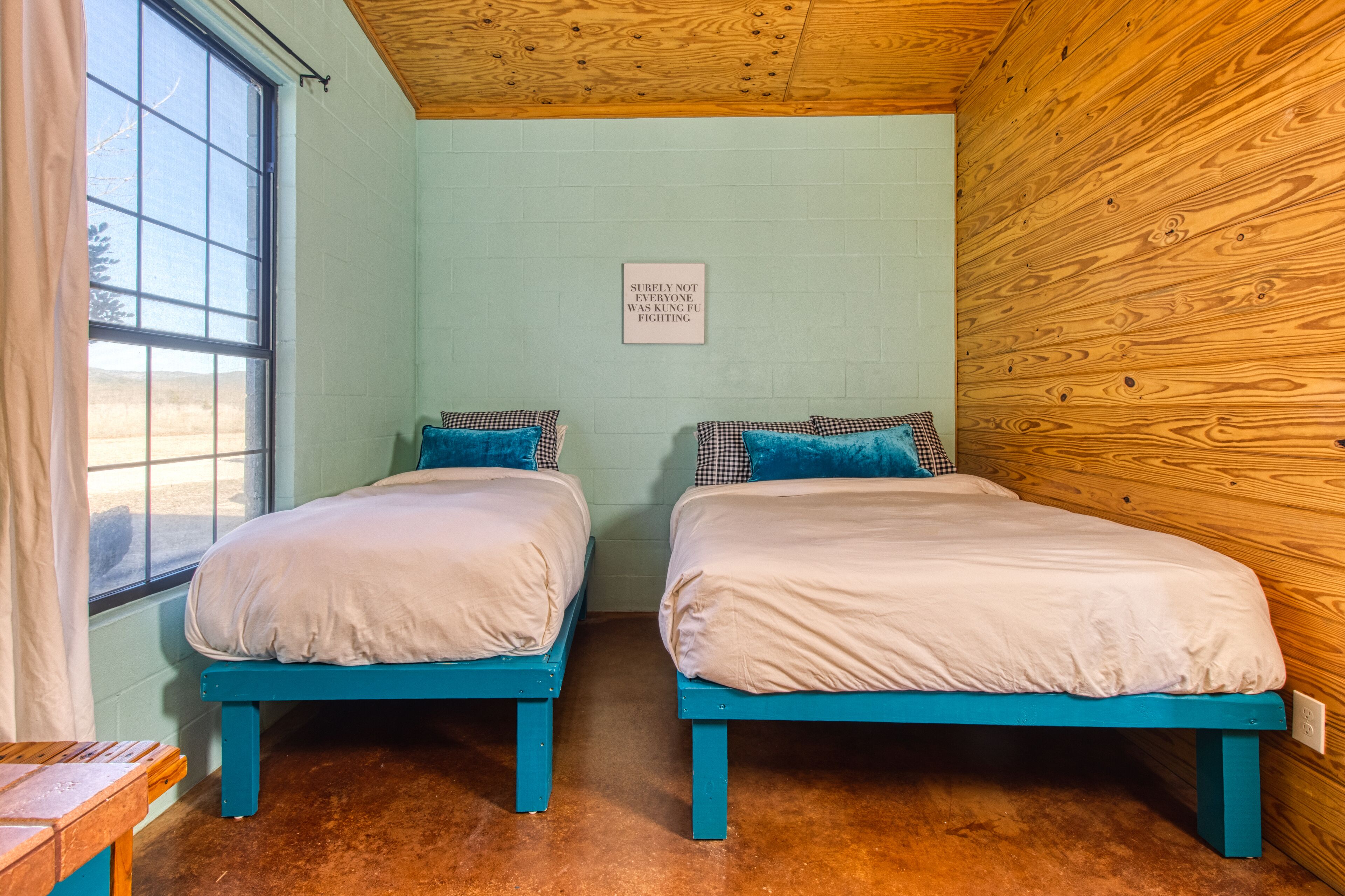 A room with two beds, a wooden ceiling, a window, and a sign on the wall.
