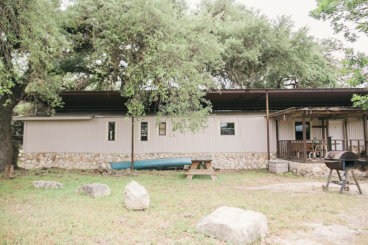 A rustic cabin with a stone foundation, a wooden deck, and a barbecue grill.