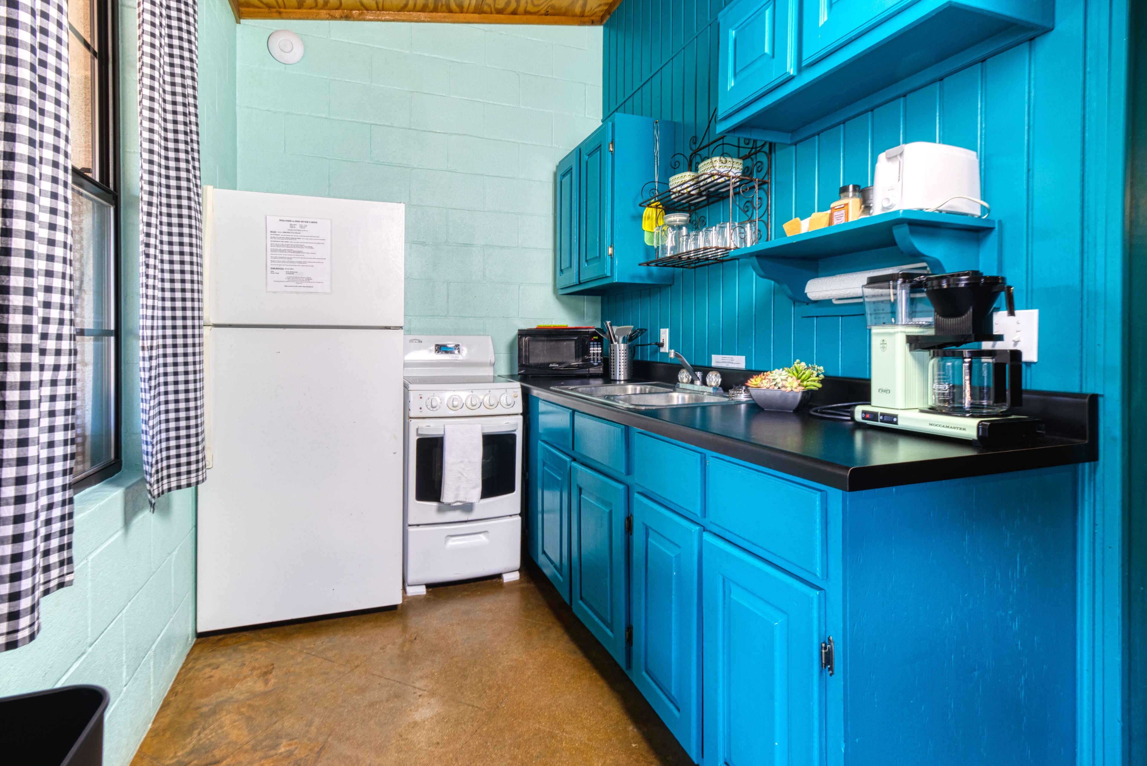 A kitchen with teal cabinets, a white refrigerator, a stove, a microwave, and a coffee maker.
