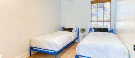 Un dormitorio con dos camas, un ventilador de techo, una ventana con persianas y una mesita con una planta.