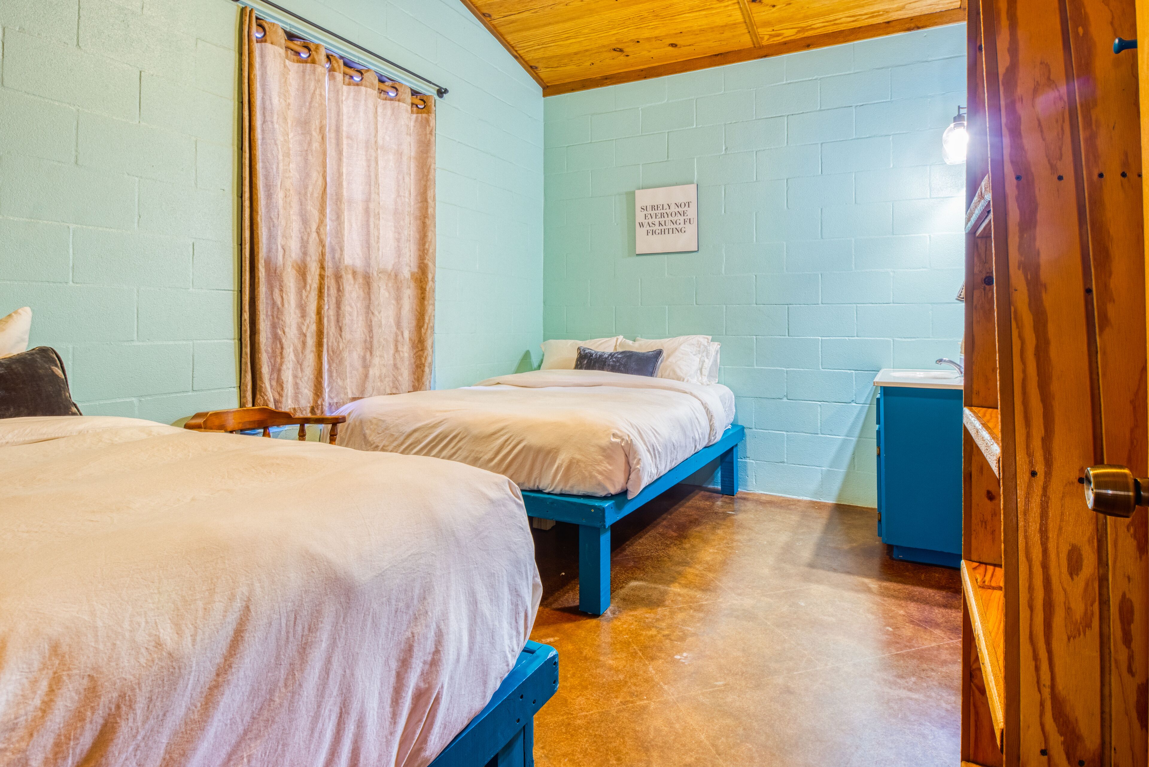 Una habitación con dos camas, un banco azul, una mesita pequeña y un armario azul.
