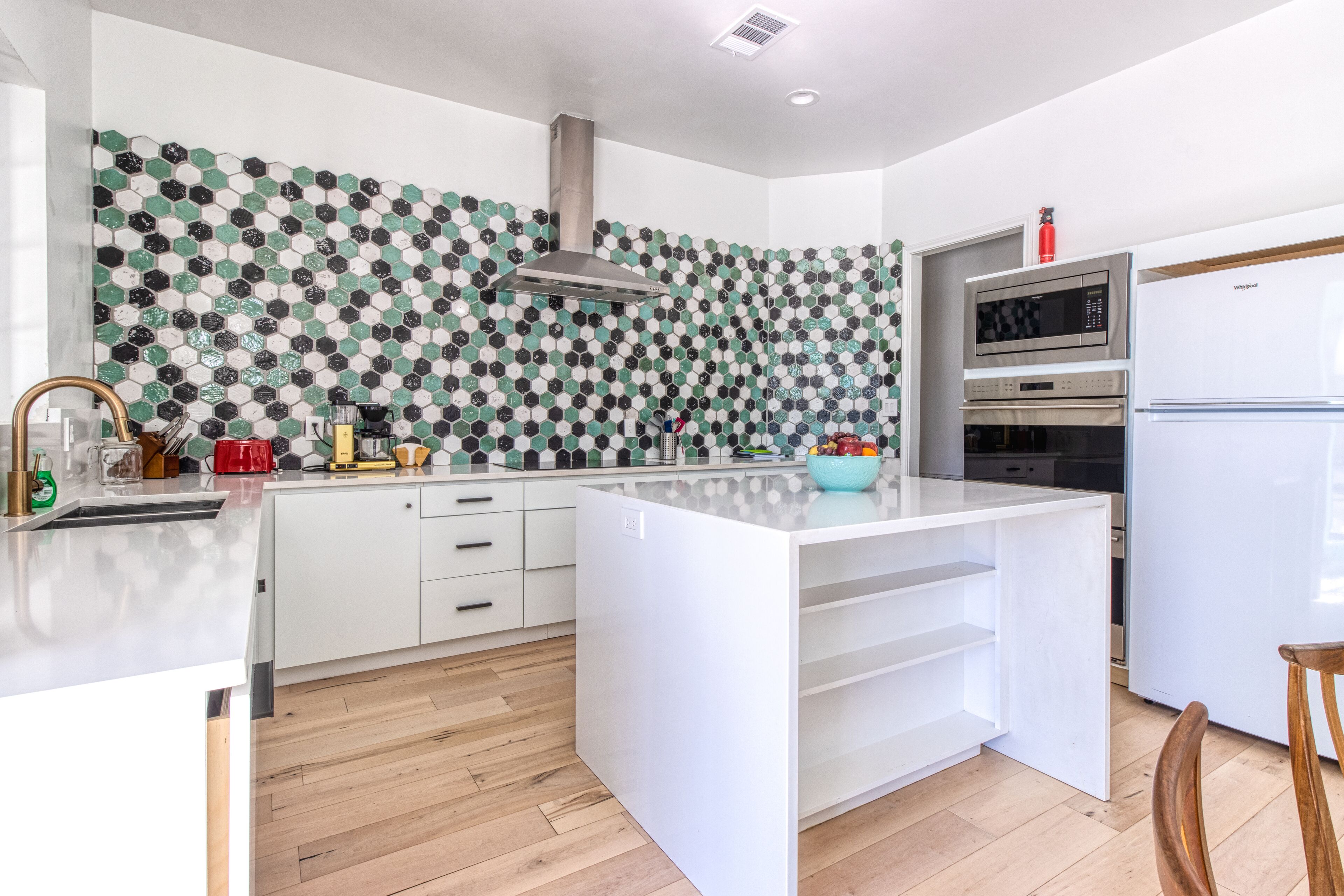 Una cocina moderna con una isla central, armarios blancos, salpicadero estampado y electrodomésticos integrados.