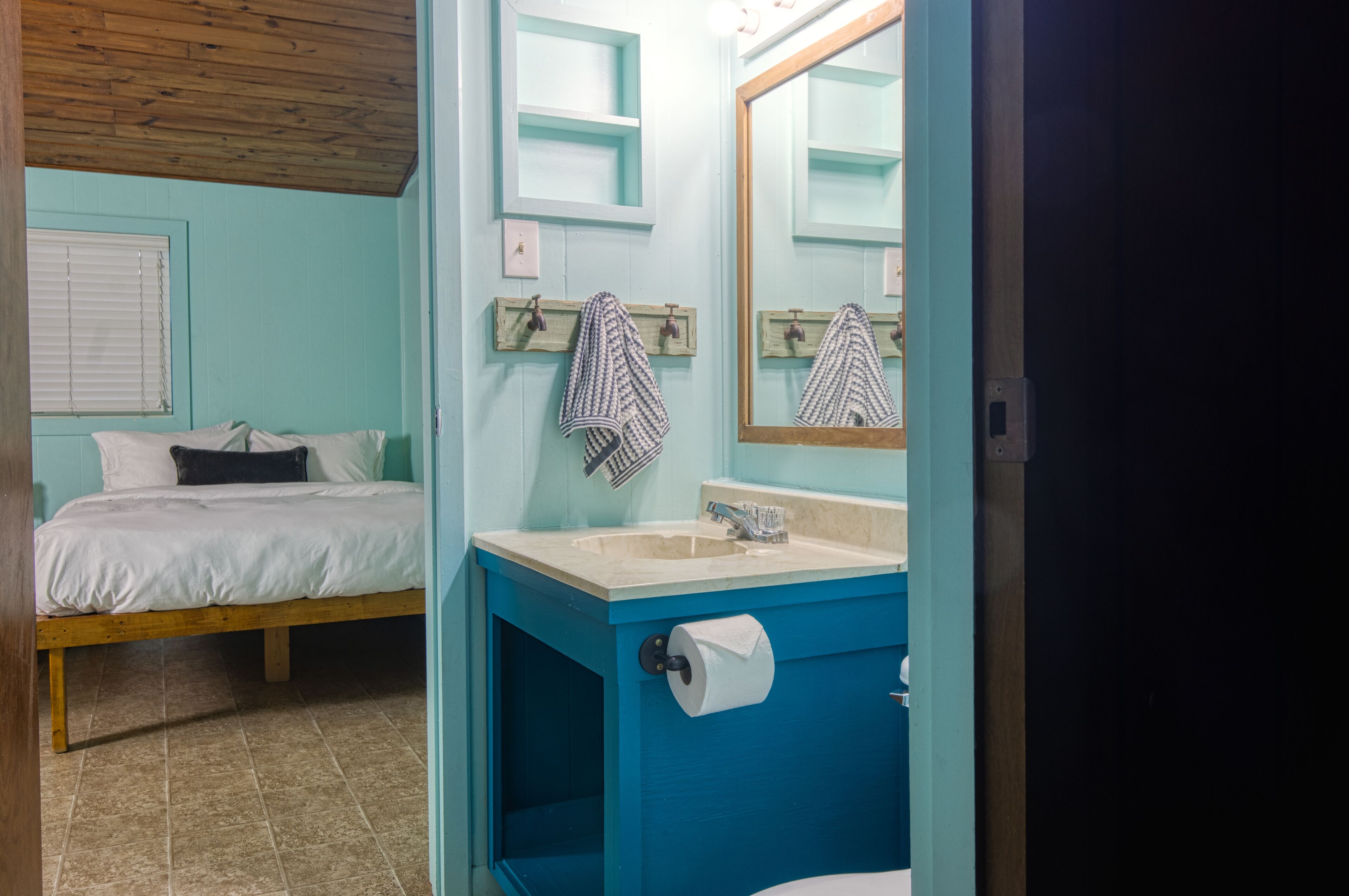 Una habitación con cama, un lavamanos azul y un espejo.