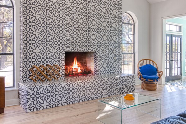 A living room with a patterned fireplace, a glass coffee table, and a wicker chair.