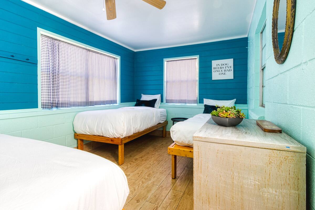 A room with two wooden beds, a small table with a bowl of fruit, and a sign on the wall.