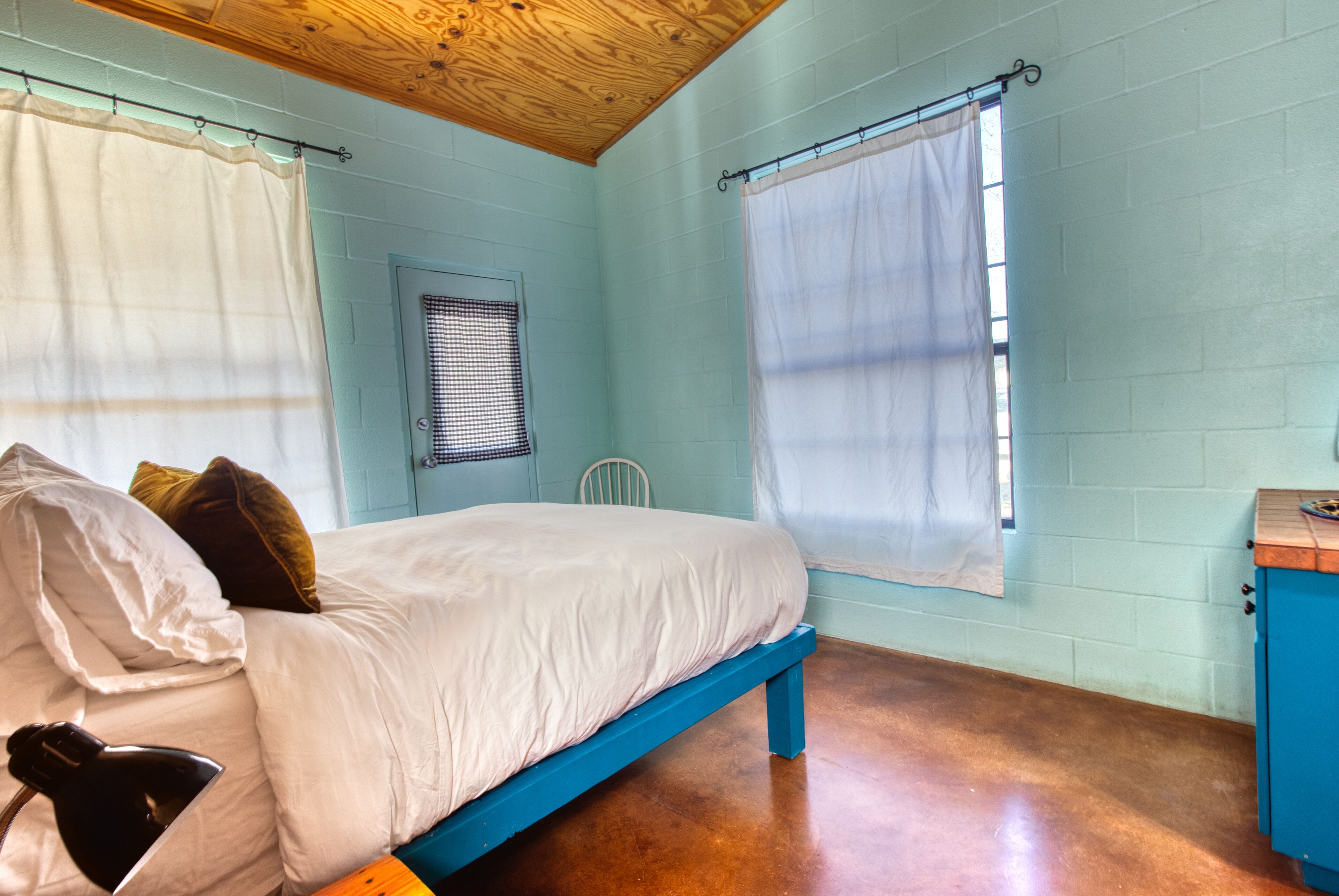 A bedroom with a bed, a desk, a chair, and a window with curtains.