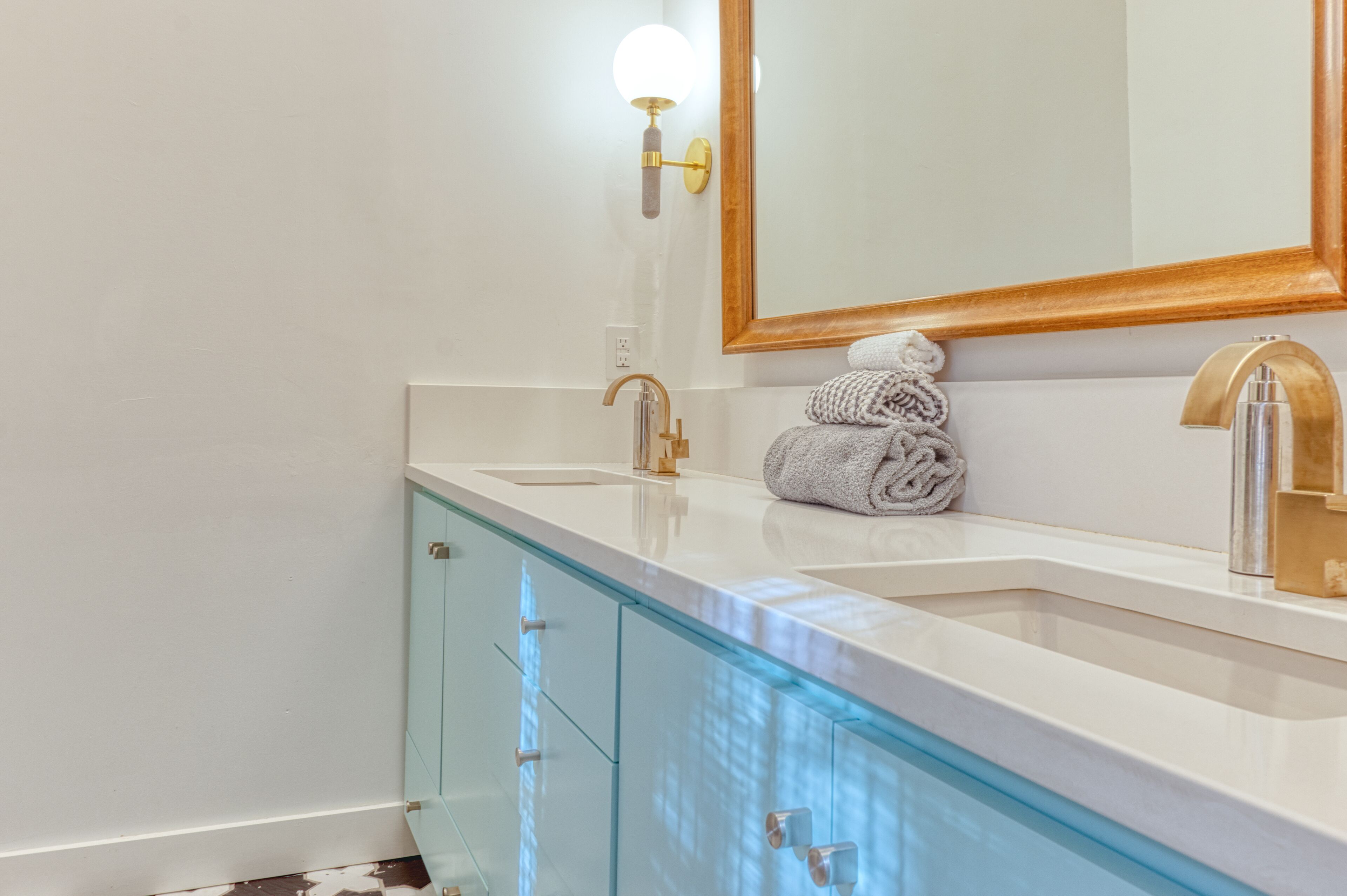 Een badkamer met een witte wastafel, een gouden kraan en een glazen kastje.