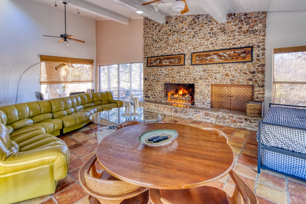 A living room with a stone fireplace, a green leather sofa, and a round wooden table.