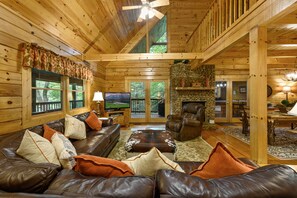 A wooden cabin interior with a leather sofa, a stone fireplace, and a television.