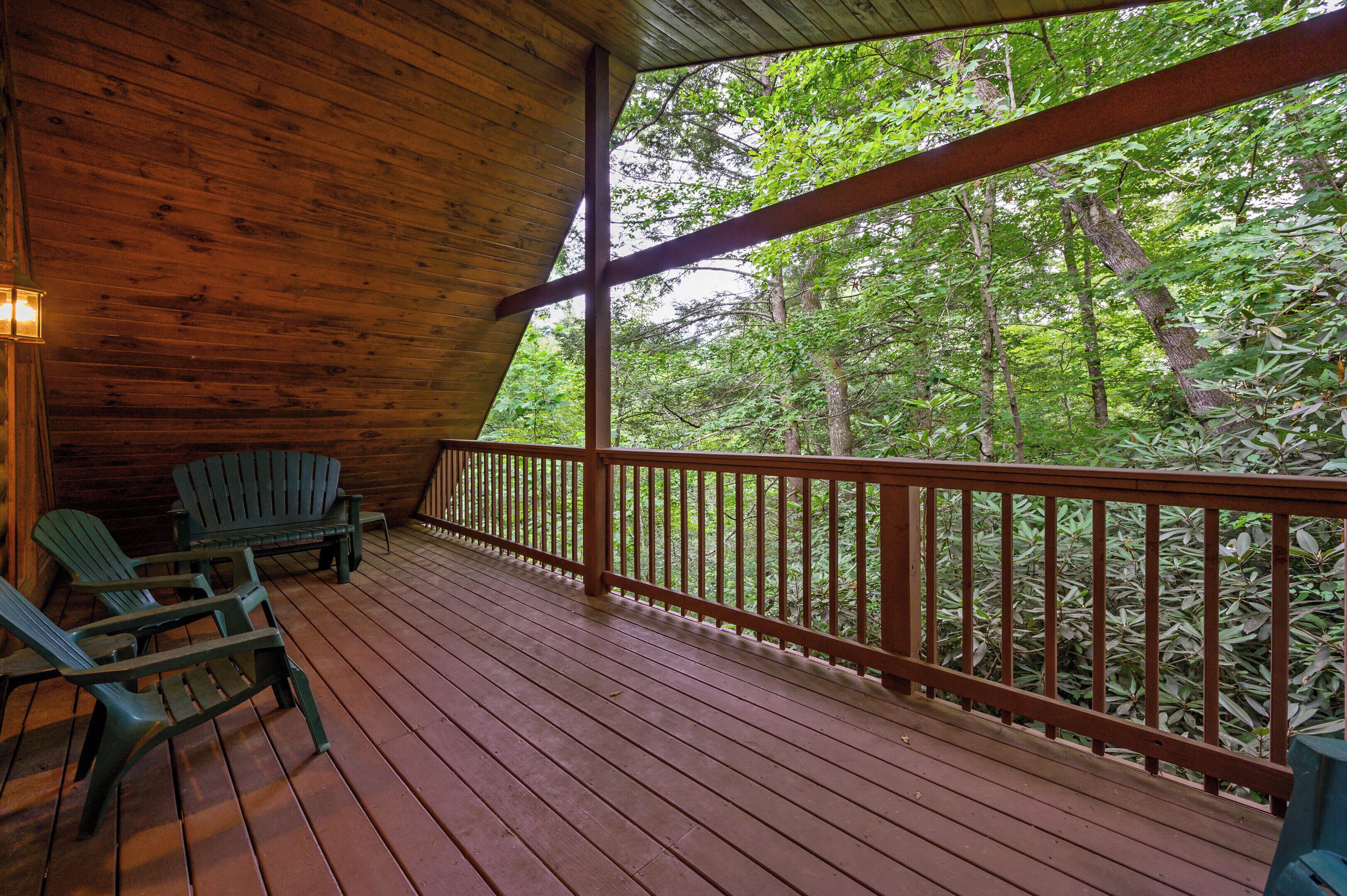 A wooden deck with a railing, green Adirondack chairs, and a view of dense trees.