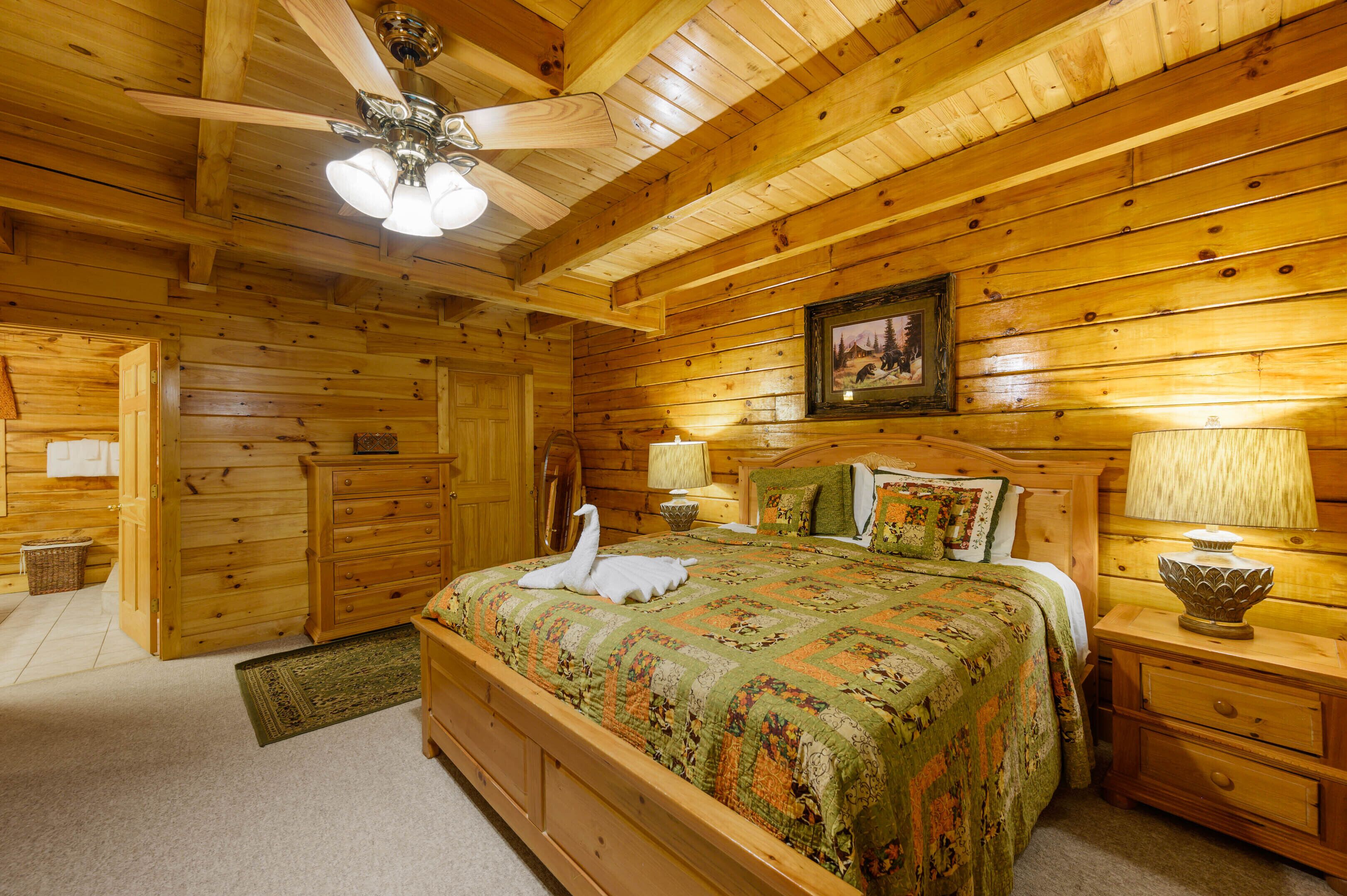 A wooden cabin bedroom with a bed, nightstands, a ceiling fan, and a framed picture on the wall.
