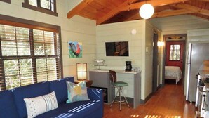 A cozy living room with a blue sofa, wooden floors, and a kitchen area with a refrigerator and a sink. - Fabulous Cabin Near Falls, Hiking, and Fly-Fishing (Brevard)