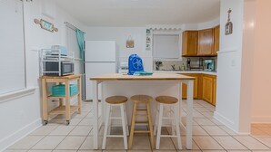 A kitchen with a central island, wooden stools, a microwave, and a refrigerator. - Beach Babe -  3/2 1st Floor Dog Friendly (Duplex) (Galveston)