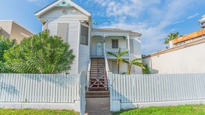 A two-story house with a front porch, a staircase leading to the entrance, and a fenced yard. - Beach Babe -  3/2 1st Floor Dog Friendly (Duplex) (Galveston)